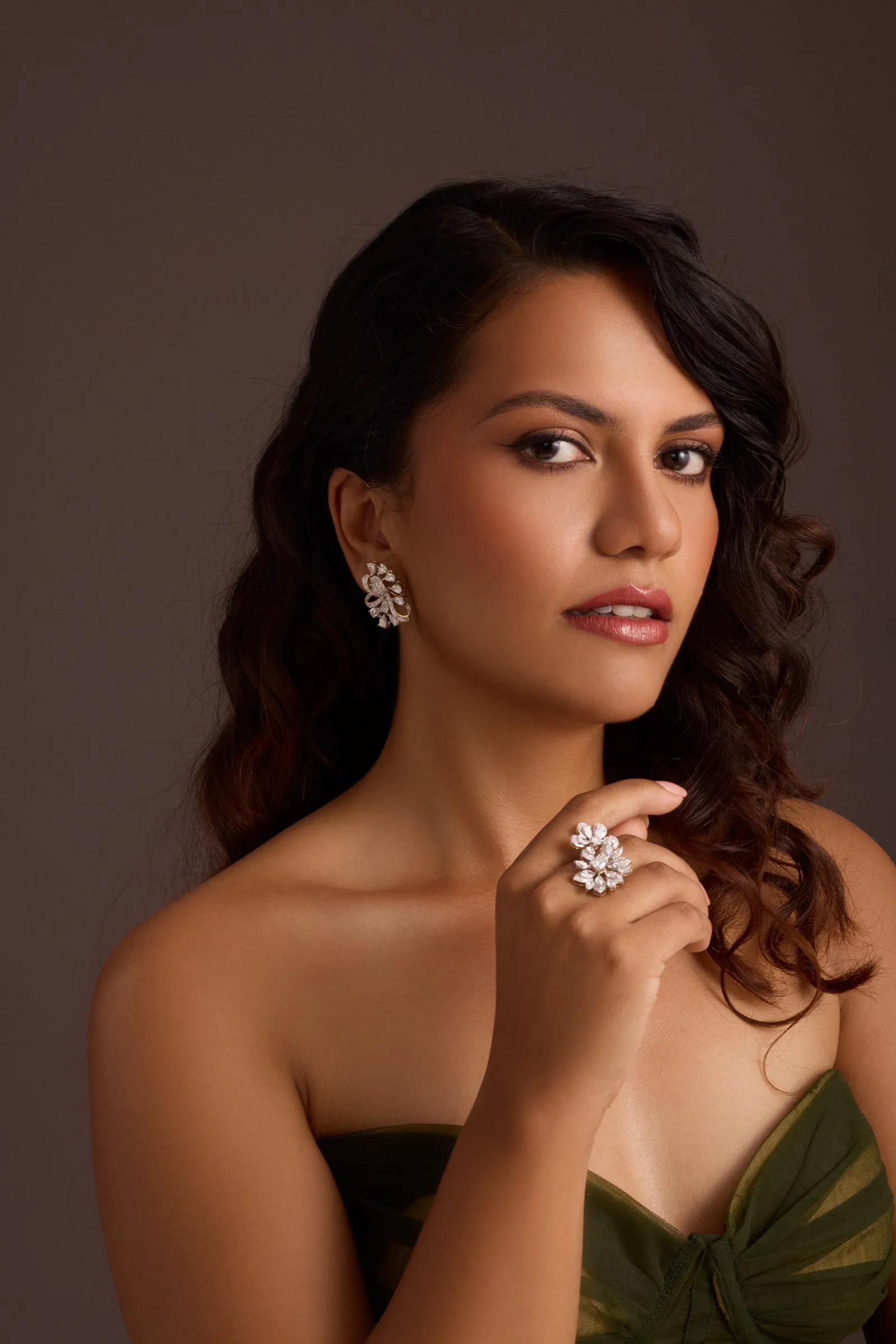 Portrait of a woman in a deep green dress wearing a Tuisa statement ring and earrings, lit against a dark background