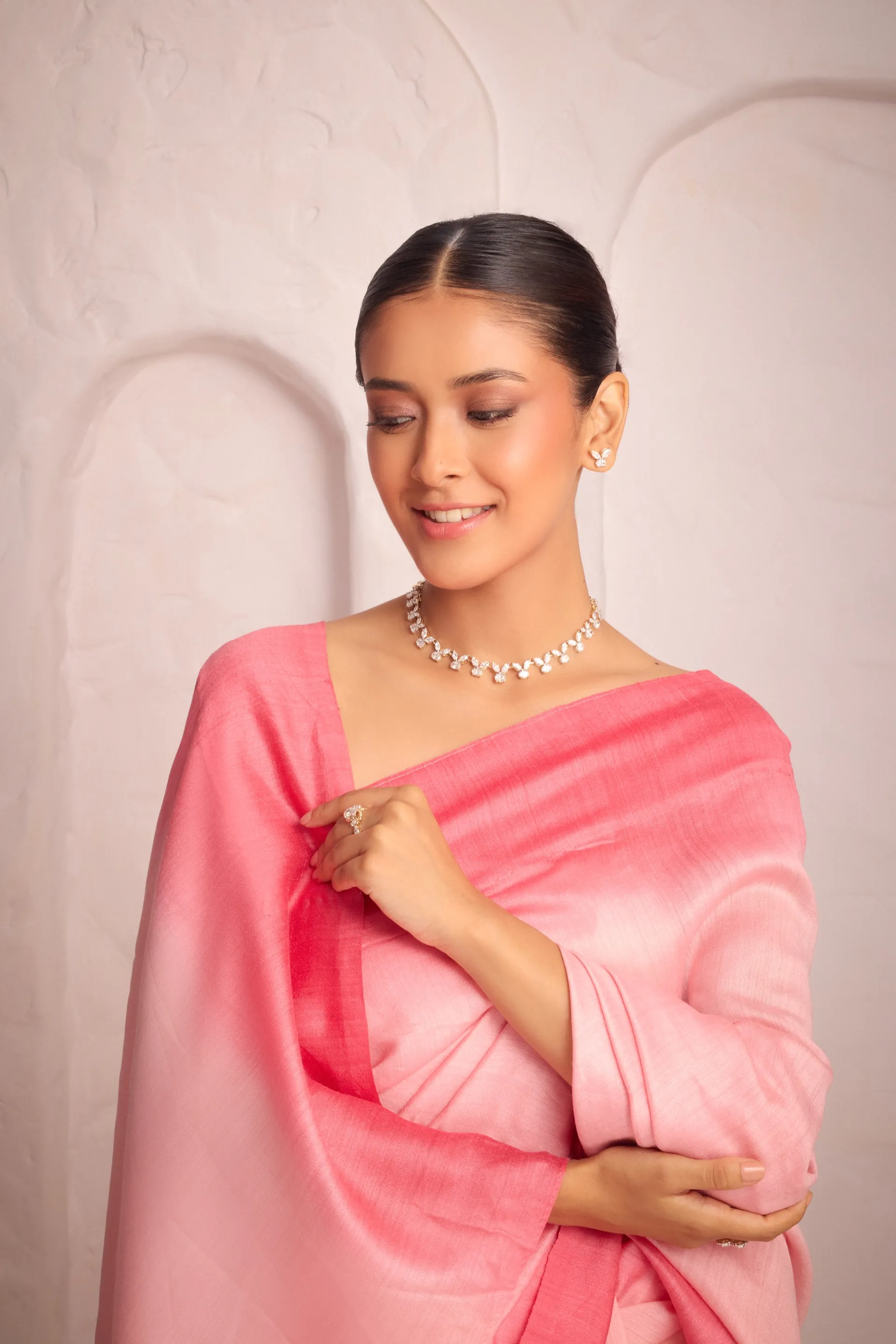 Model in a pink sari wearing a Tuisa diamond necklace, smiling softly against a sculpted ivory wall