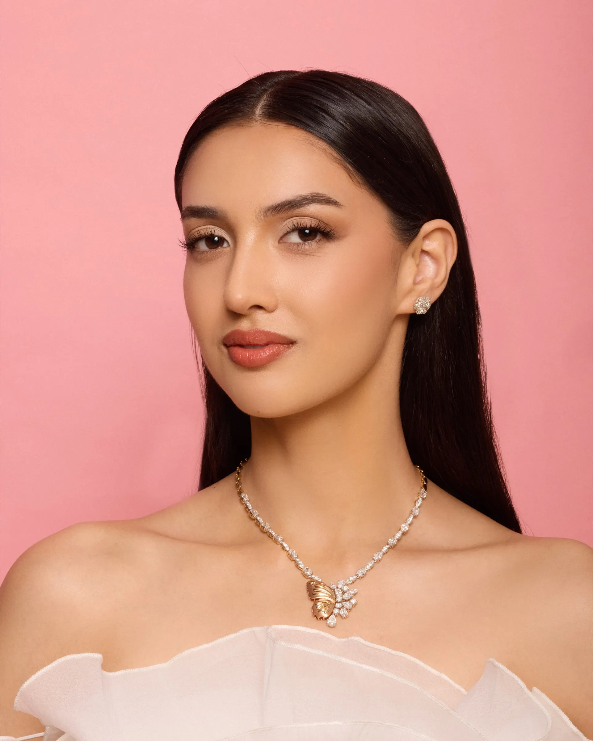 Model wearing a Tuisa diamond butterfly necklace against a coral backdrop