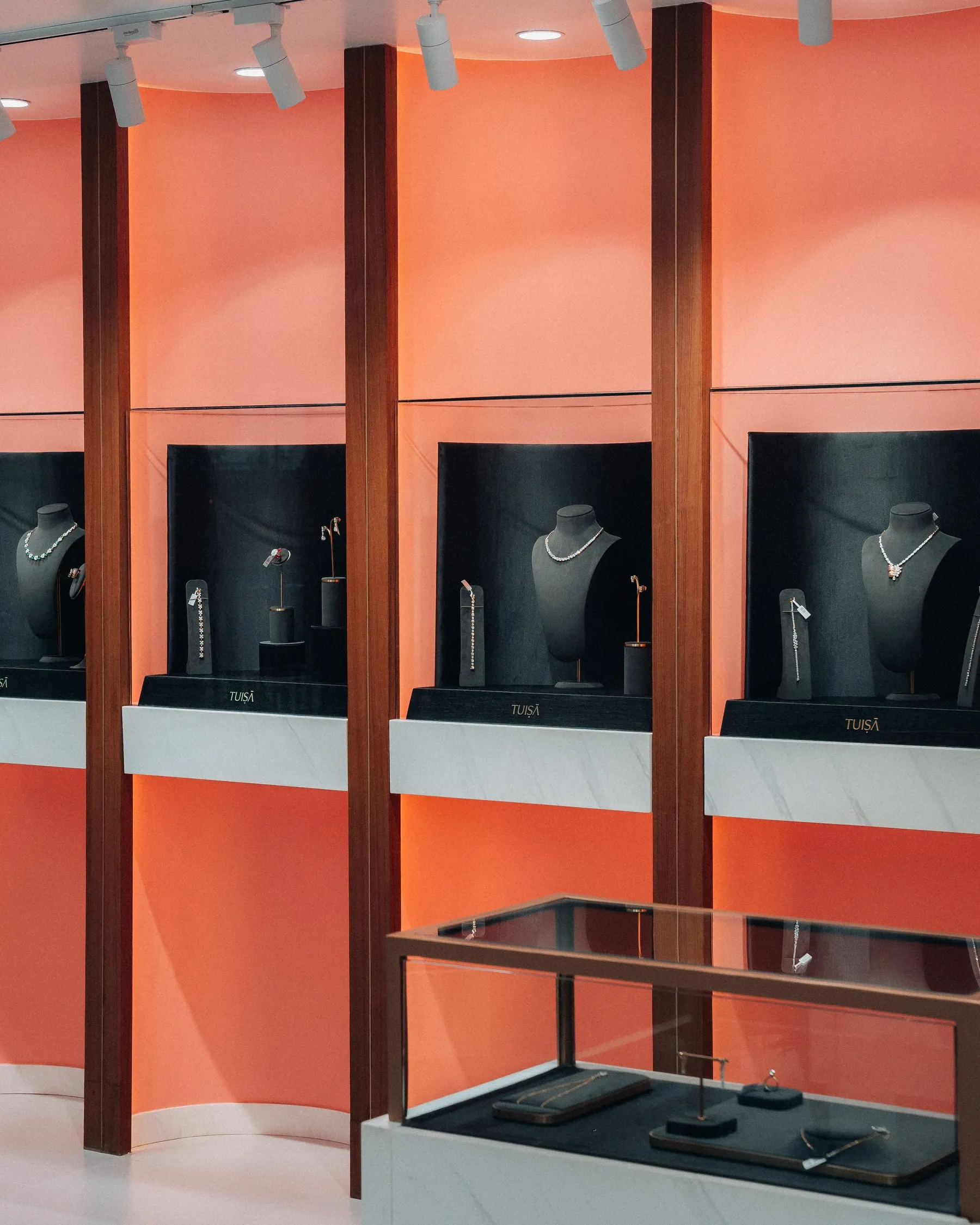 Necklaces on display against the coral vitrine wall of the Tuisa boutique